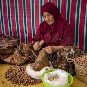 A woman shells Argan nuts to make oil near Morocco's western Atlantic coastal city of Essaouira, on October 15, 2022. - Morocco's argan oil is highly prized by the cosmetics industry, yet it is now mostly produced by elderly workers, raising questions about how long the artisanal practice can continue. (Photo by FADEL SENNA / AFP)